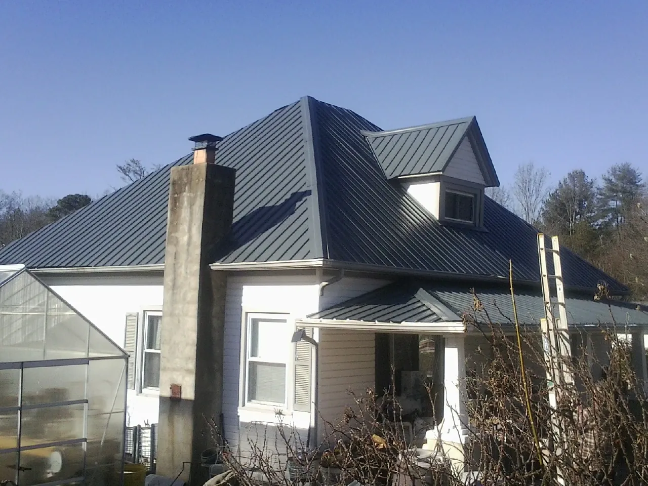 Dark blue standing seam metal roof on a white farmhouse with dormer — Slate & Tile Roof Repair by Roofing Brothers in Nerstrand