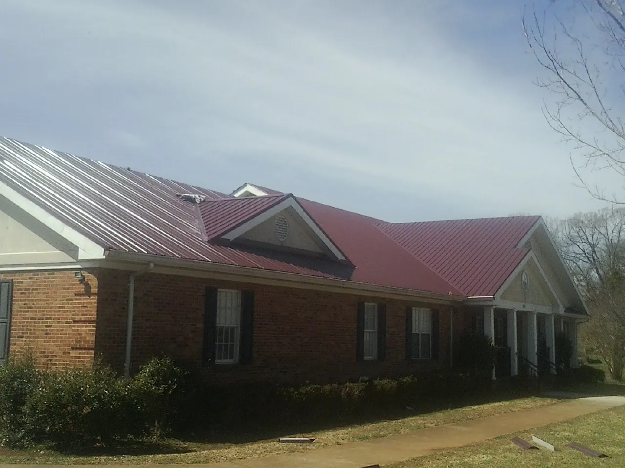 Red metal roof with gabled entries on a long brick building, from a Hail Damage Roof Repair job in Nerstrand