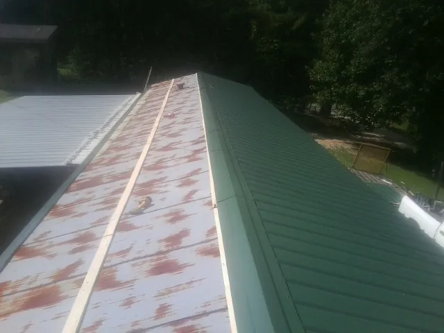 Old rusted panels beside newly installed green metal roofing — Wind Damage Roof Repair by Roofing Brothers in Nerstrand