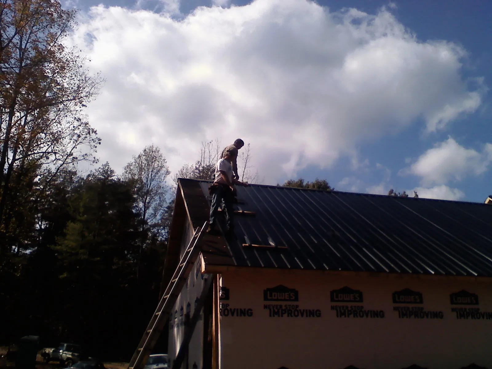 Roofer fastening dark metal panels high against a cloudy sky, from a Roof Inspection job in Nerstrand